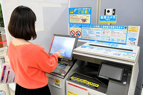 コンビニのコピー機で交付操作をする人